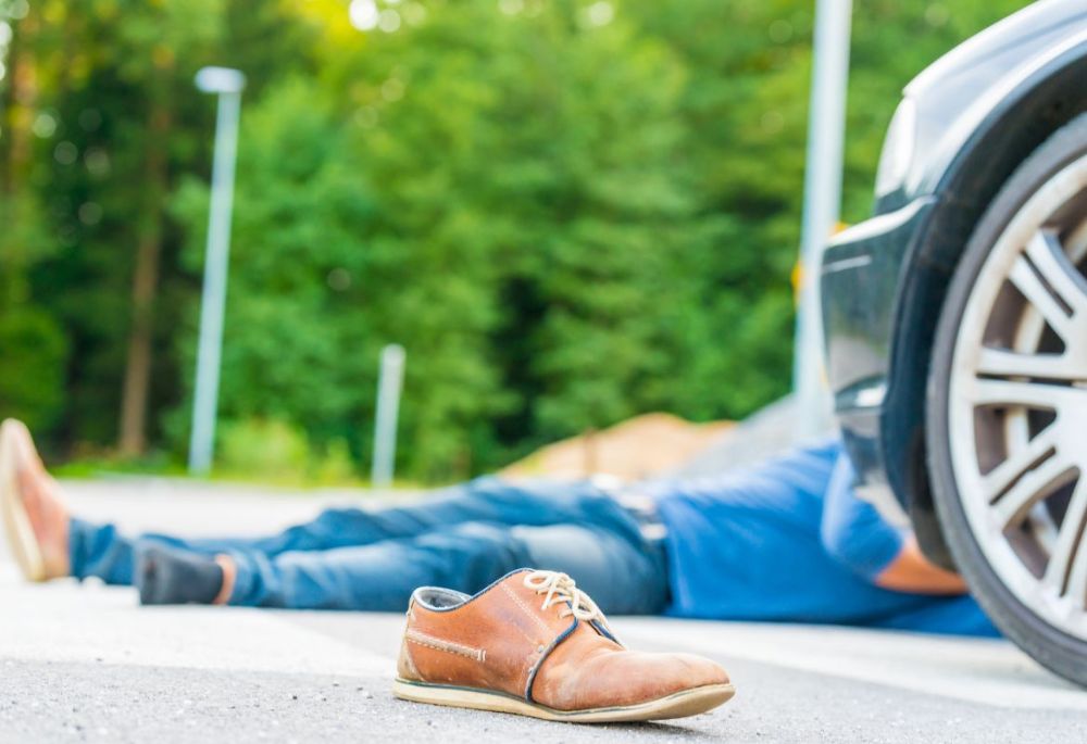 Pedestrian Accident Brown shoe and injured person lying on ground beside car