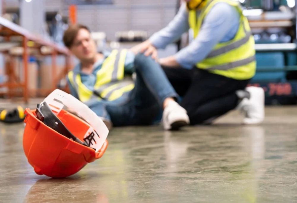 Workplace Accident A man in a safety vest and helmet sits on the floor, indicating a workplace accident
