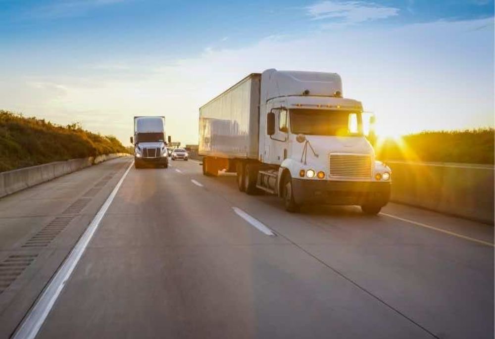 Trucks Two semi trucks drive down a highway at sunset