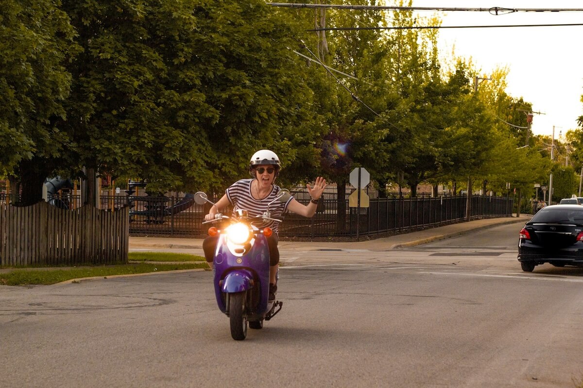 Woman Riding a Scooter and Waving at the Camera