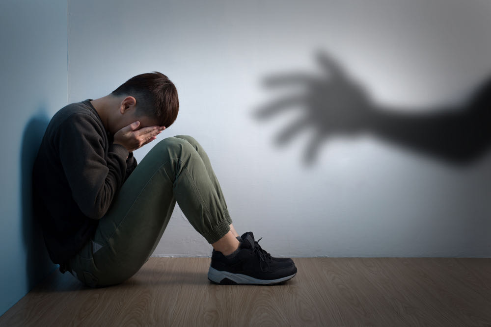 Depressed Man Man in depression sitting in the corner and a visible shadow hand is seen on the wall